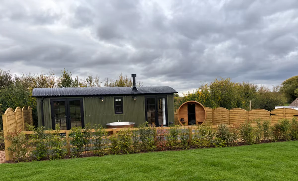 Sloe's olive cabin, copper bath and barrel sauna beyond the garden hedge